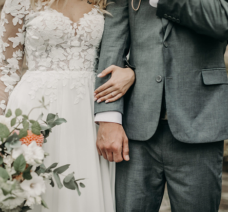 Brudpar i bröllopskläder som håller armkrok, med bukett i förgrunden, fotograferat vid Egastronomi.