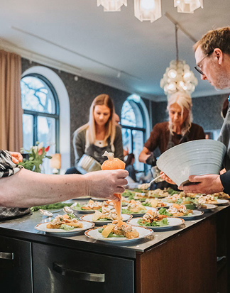 Personer serverar mat tillsammans under en kickoff med gemensam matlagning i modern restaurangmiljö.